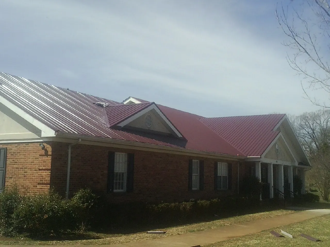 Red metal roof with gabled entries on a long brick building, from a Hail Damage Roof Repair job in Valles Mines