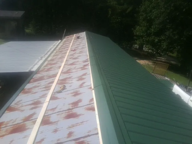 Old rusted panels beside newly installed green metal roofing — Wind Damage Roof Repair by Roofing Brothers in Valles Mines