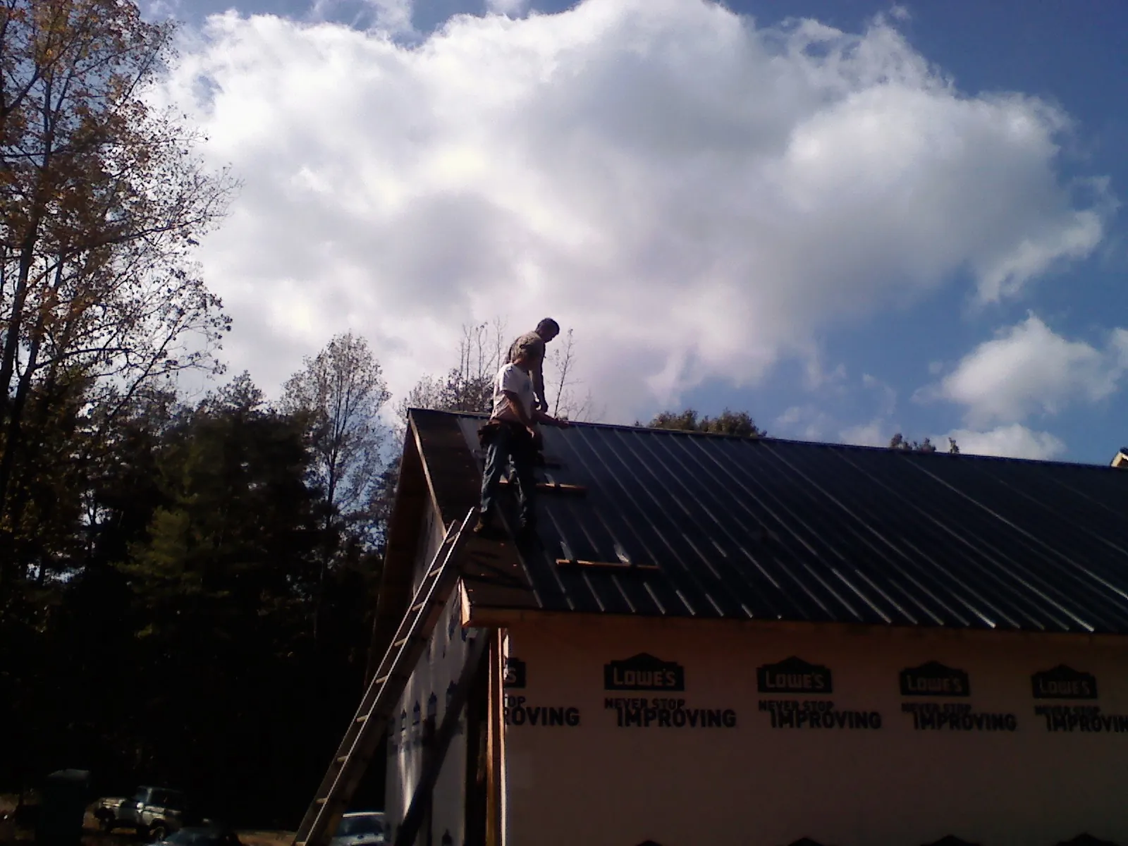 Roofer fastening dark metal panels high against a cloudy sky, from a Roof Inspection job in Valles Mines
