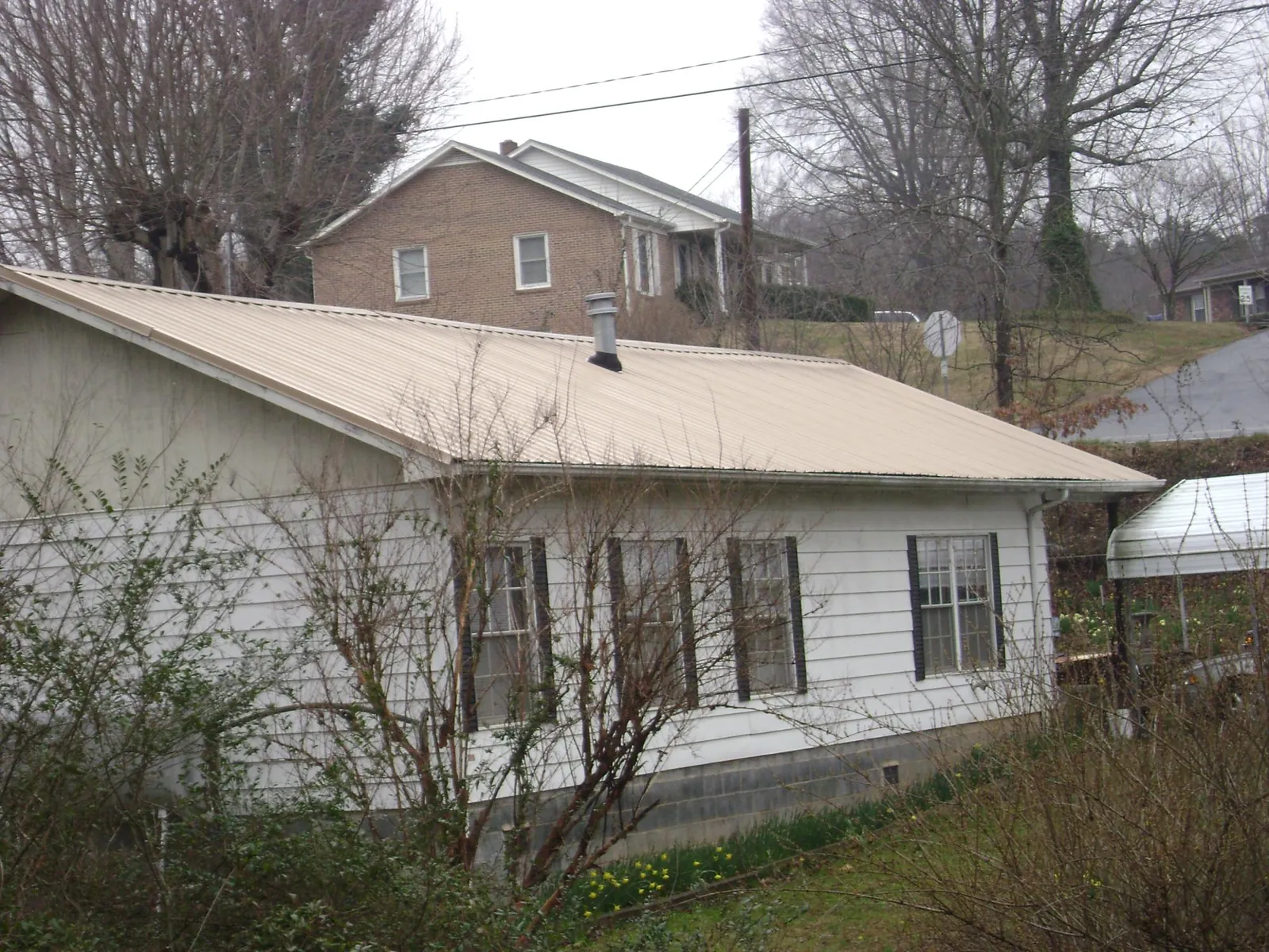 Tan metal roof on a white sided house set into a hillside — Commercial Roofing by Roofing Brothers in Valles Mines