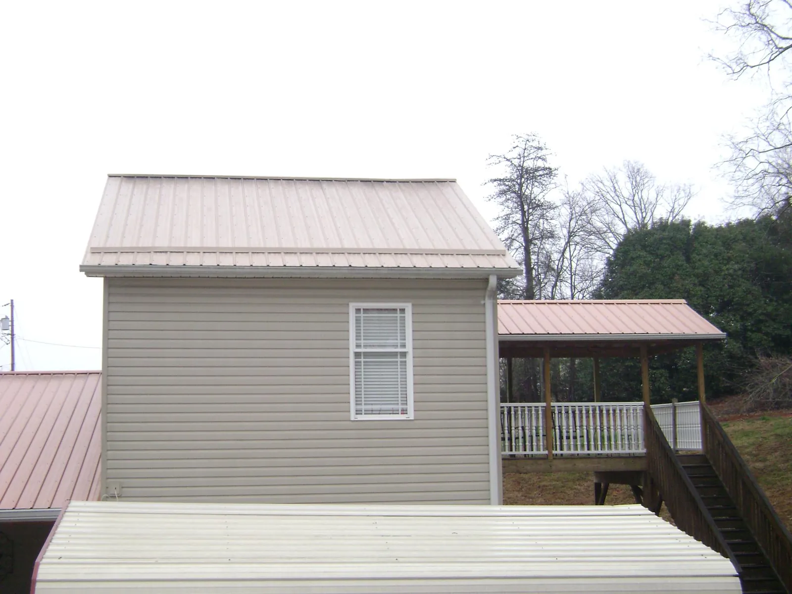 Tan metal roofs on a two story addition and attached porch, from a Roof Replacement job in Valles Mines